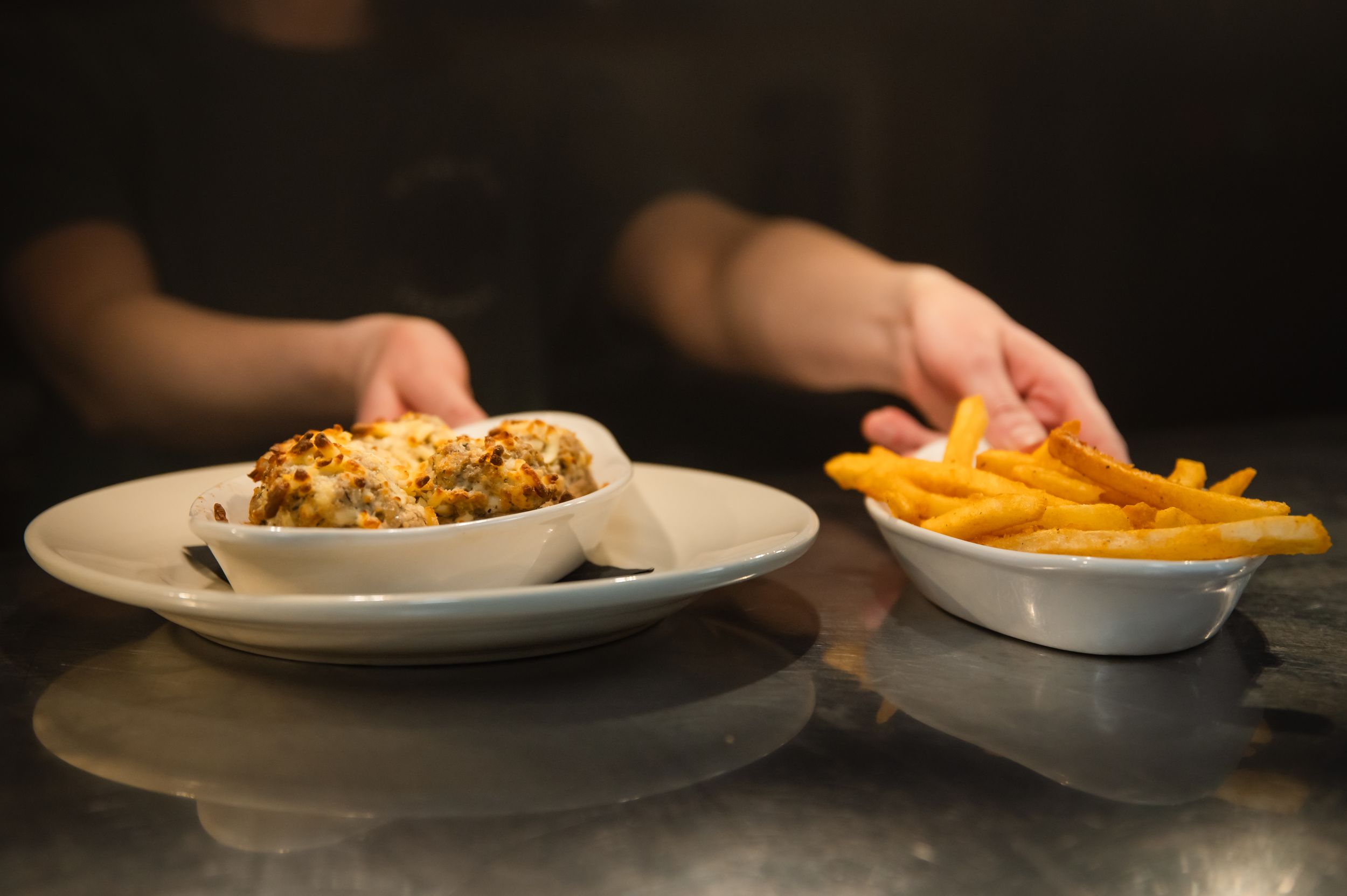 Multiple plates of food being served on a dark surface in a restaurant setting.