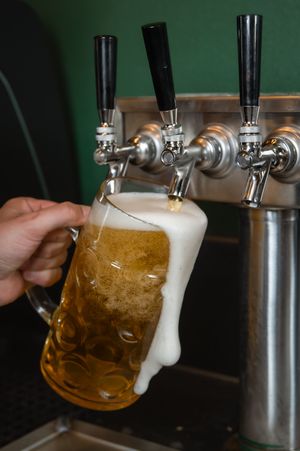Beer being poured from a draft tap into a glass mug with foam overflowing at the top.