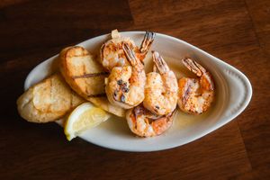 Grilled shrimp and bread appetizers arranged on white plates against a dark wooden background.