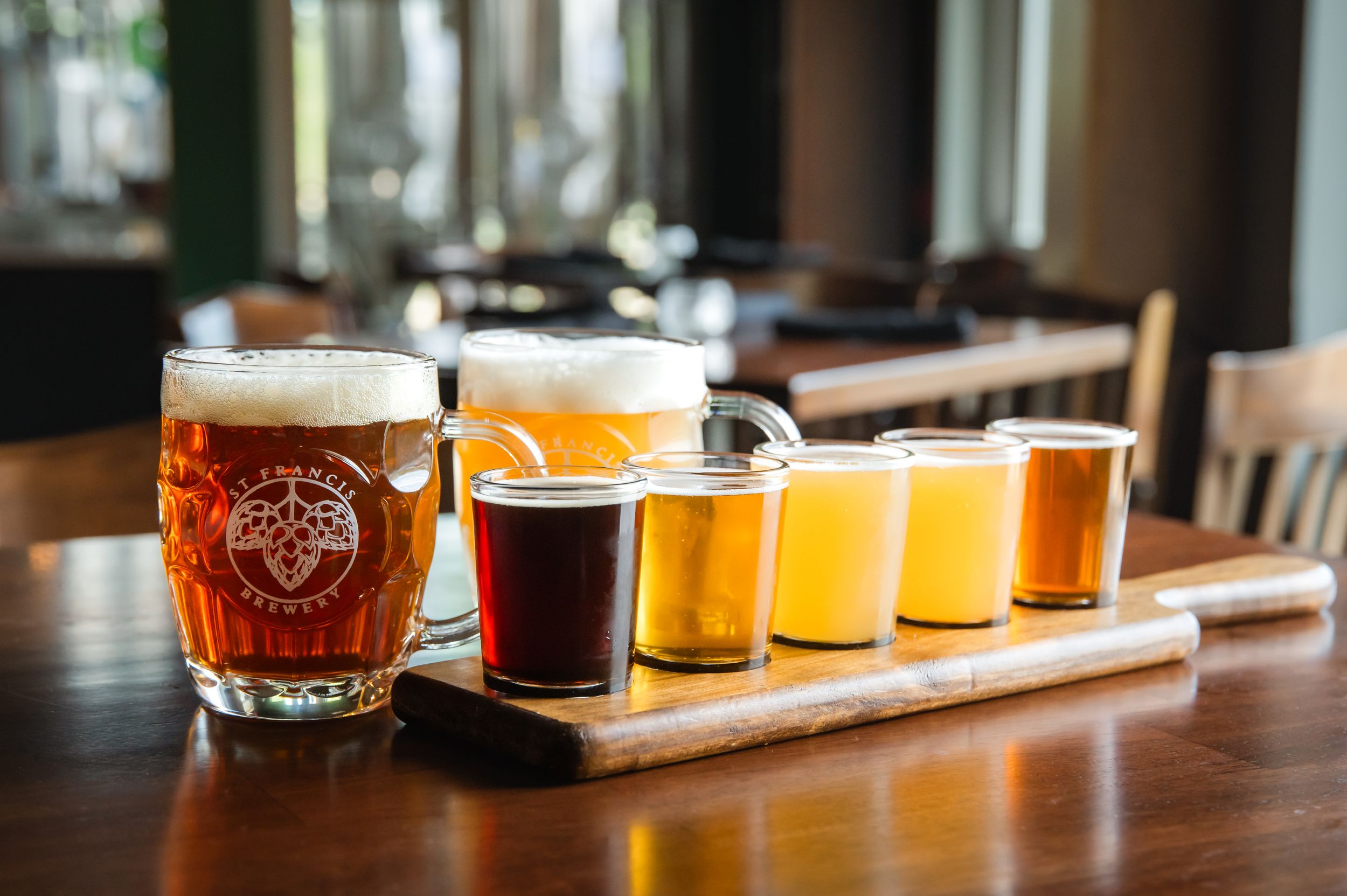 A flight of craft beer samples arranged in a row on a wooden tasting board at a brewery.
