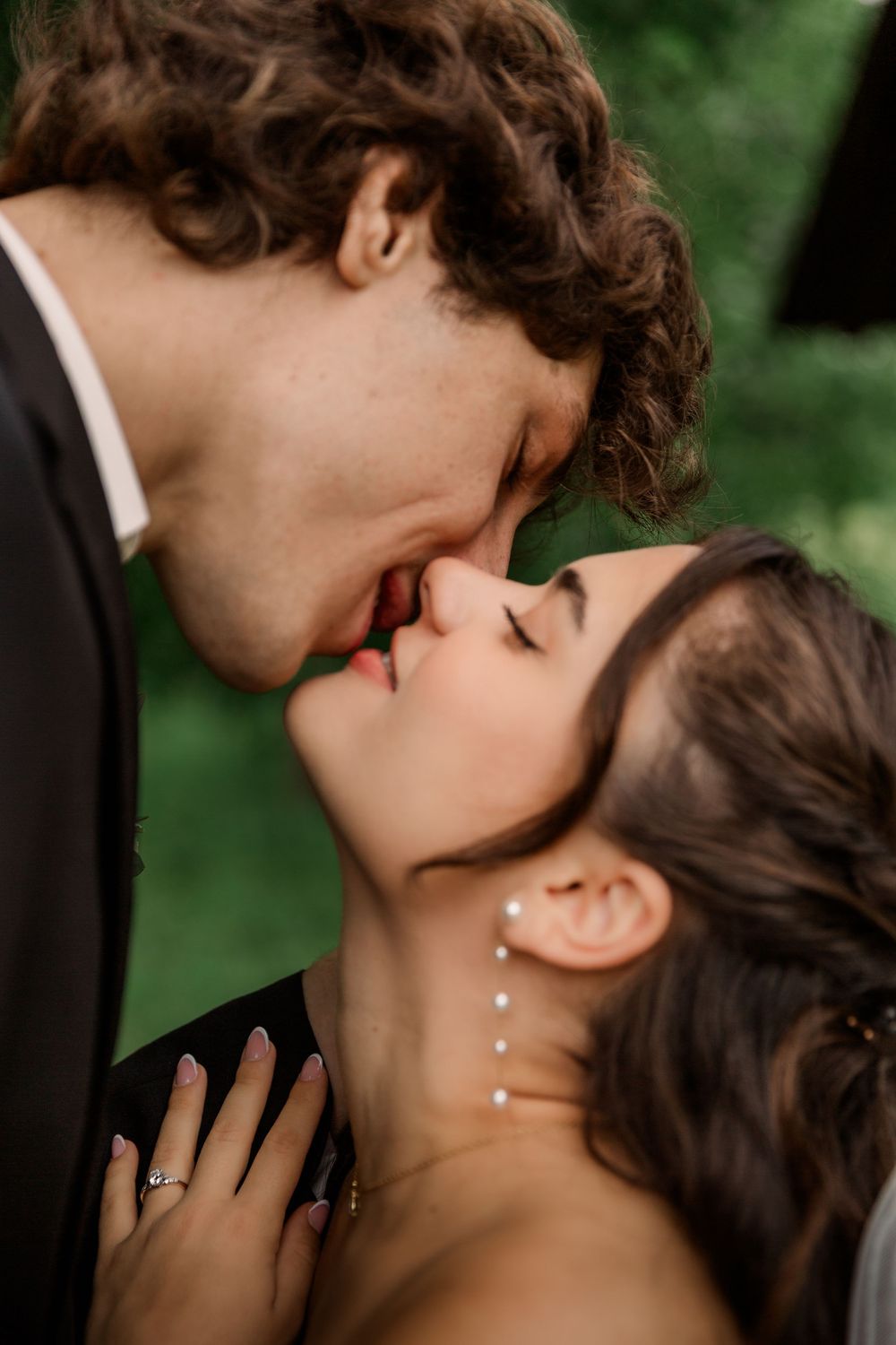 A romantic wedding kiss captured in soft natural lighting with greenery in the background.