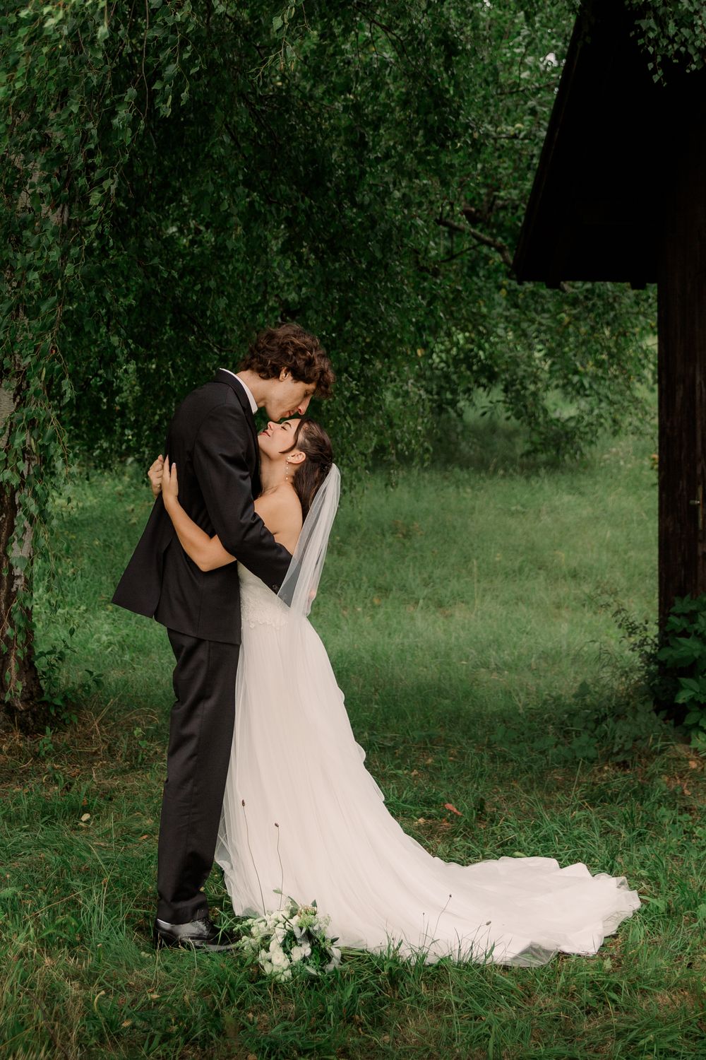 A romantic wedding couple embracing in a lush green garden setting.