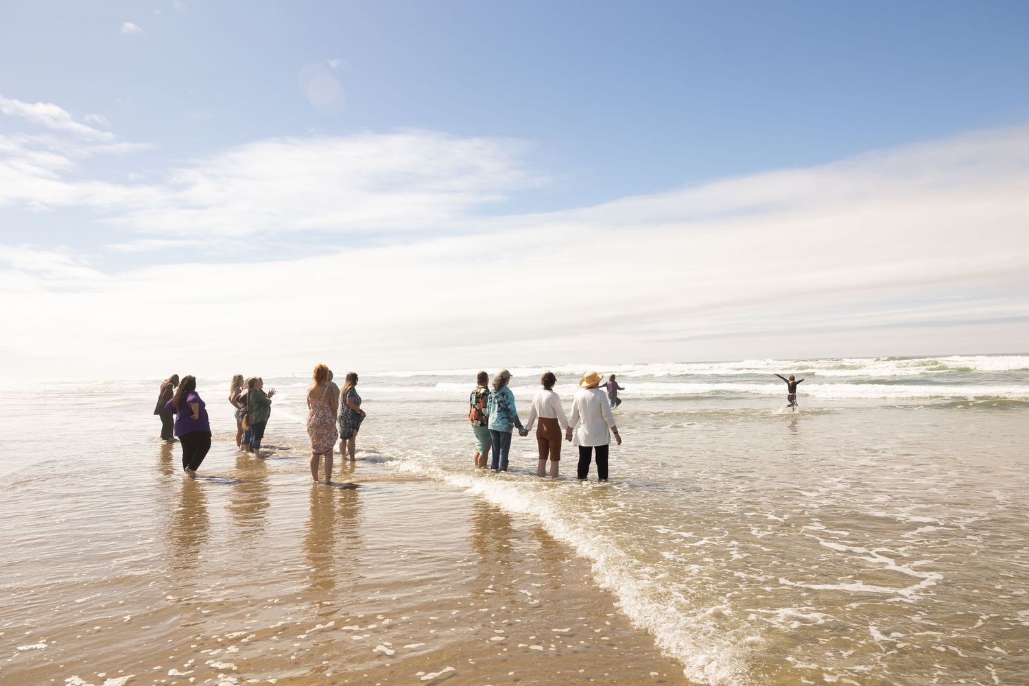 People walking along a sandy beach shoreline with gentle waves and blue sky on a sunny day.