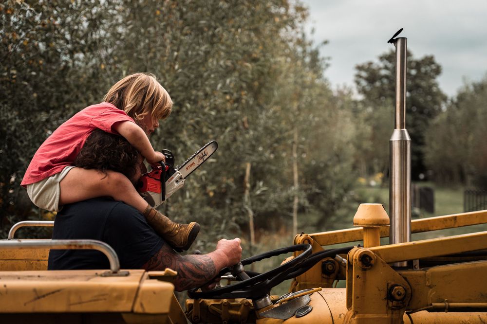Person sitting on vintage yellow tractor machinery while looking at something in their hands.