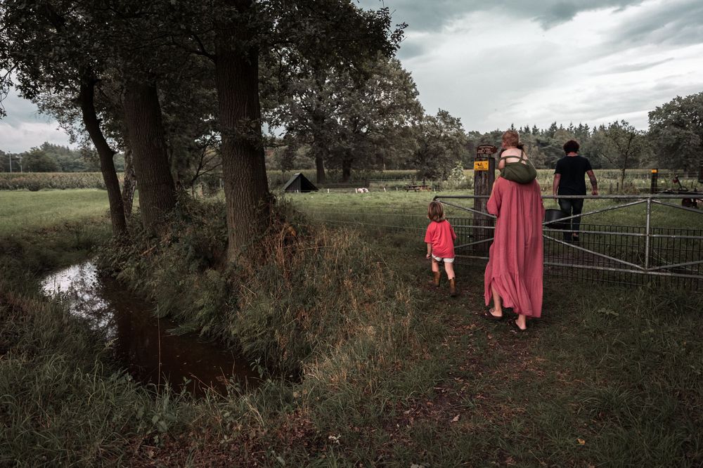 People walking along a countryside path near a pond and trees on an overcast day.