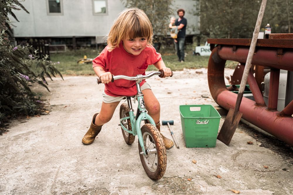 Child riding a small turquoise bicycle on a concrete path near outdoor equipment.