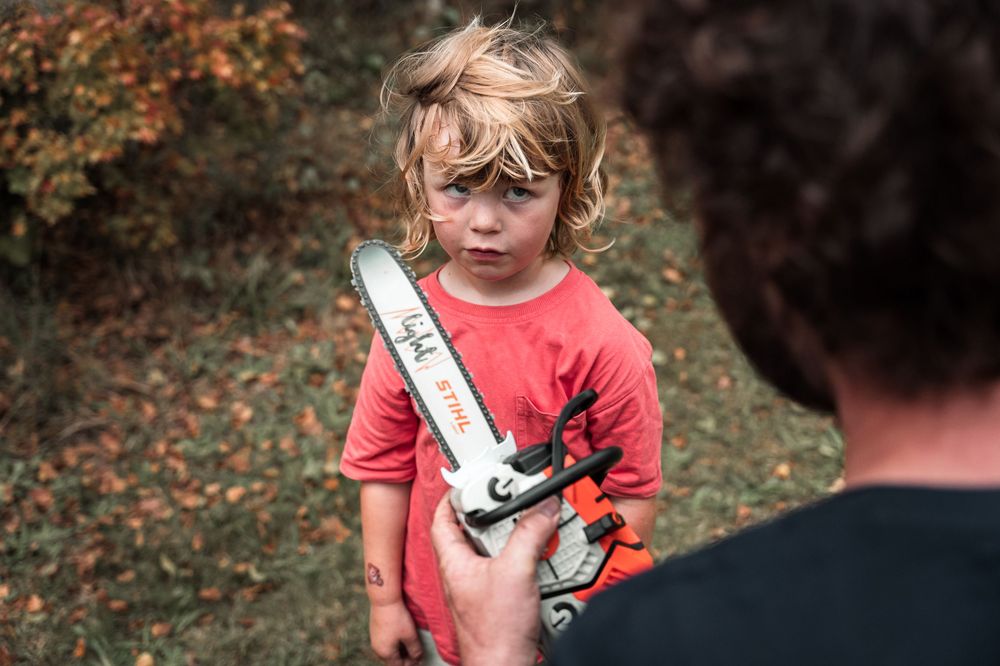 Child in red shirt holding a toy wrench tool outdoors during autumn.