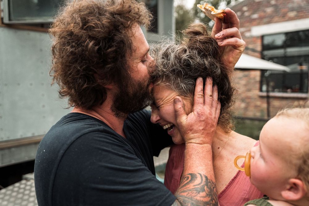 Intimate family moment captured outdoors near rustic building exterior.