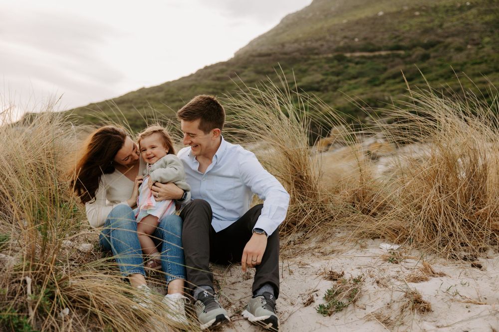 A family enjoys a candid moment together while sitting in coastal sand dunes.
