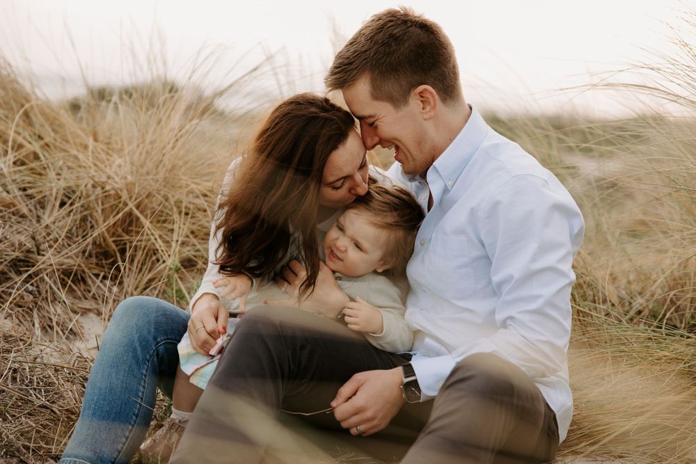An intimate family portrait captured in golden light among beach grass.
