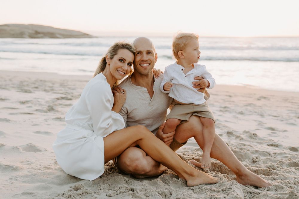 A relaxed family moment captured during golden hour on a sandy beach.