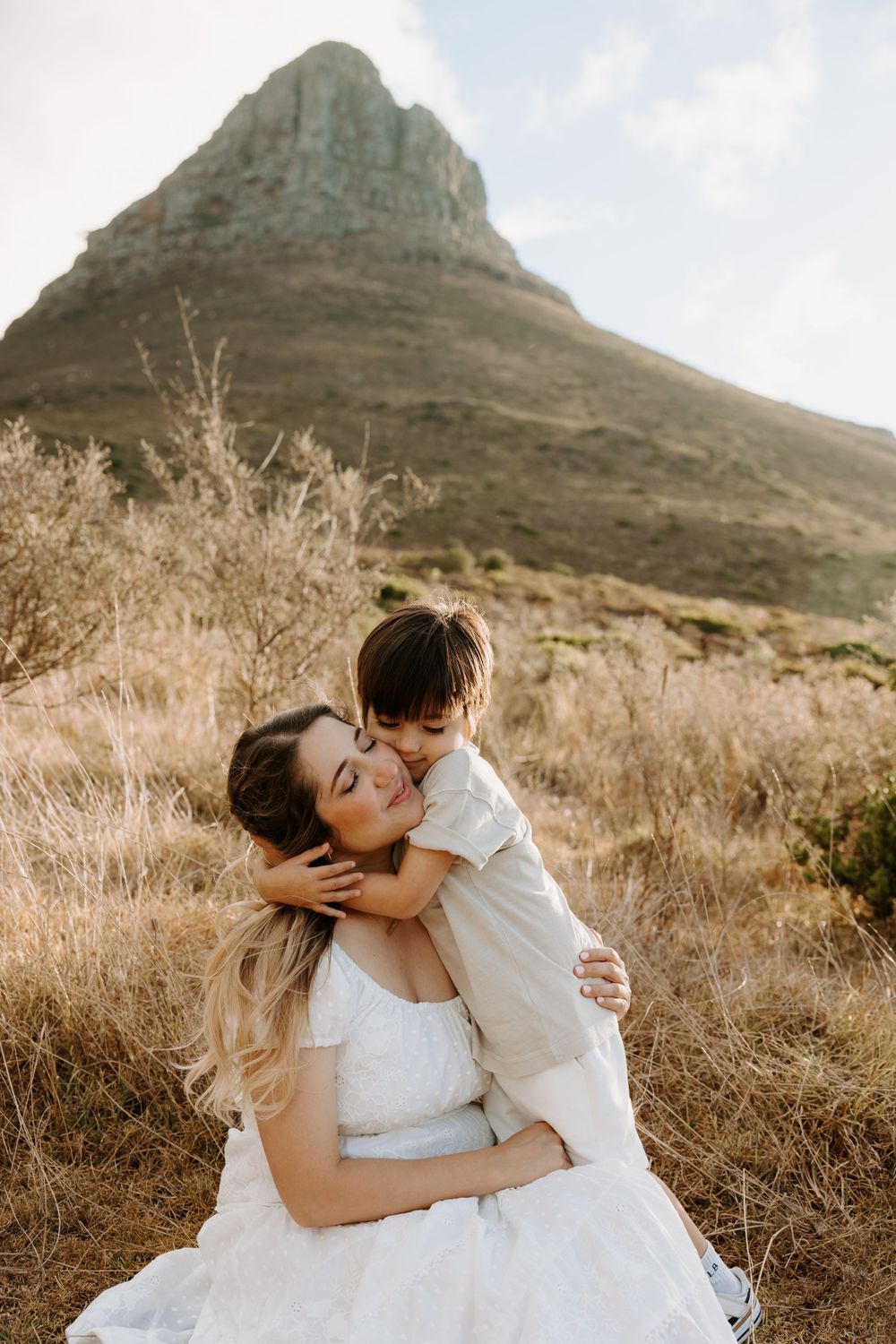 An intimate portrait against a mountain backdrop shows an embrace in white attire.