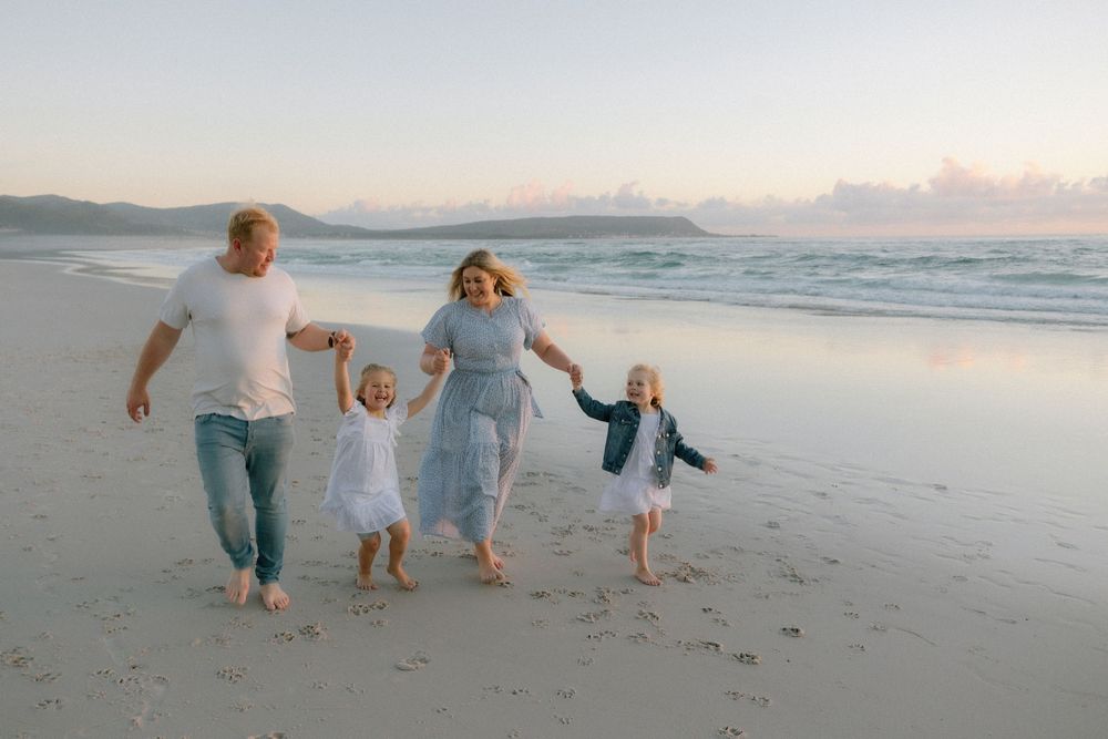 A family of four holds hands while walking together along a scenic beach at sunset.