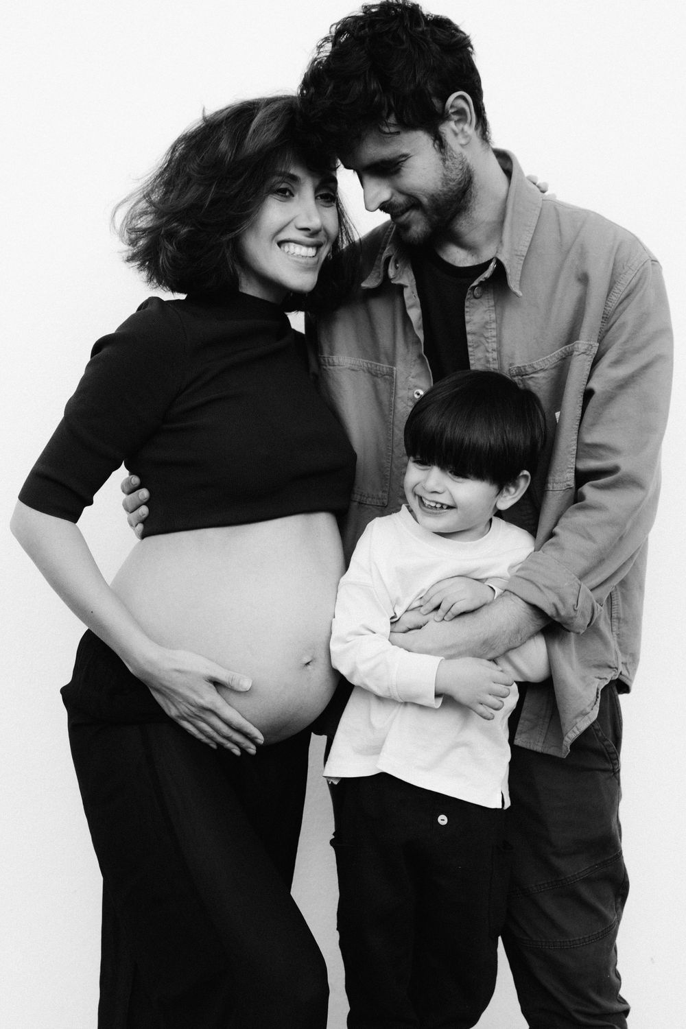 Black and white family portrait featuring expecting parents and their child.