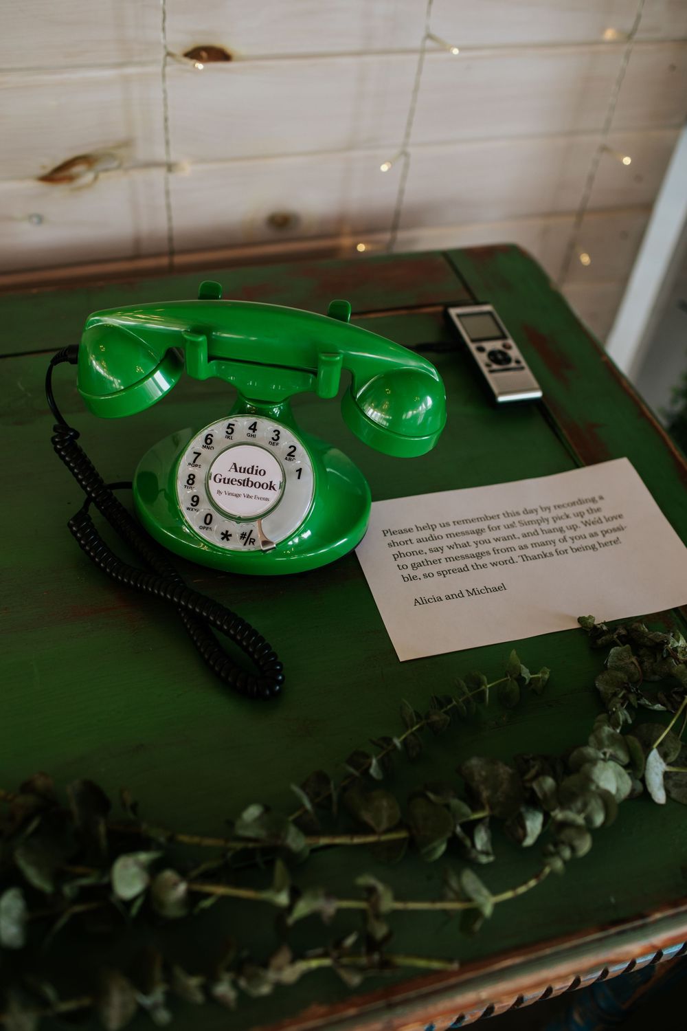 Vintage green rotary telephone displayed on dark surface with decorative greenery.