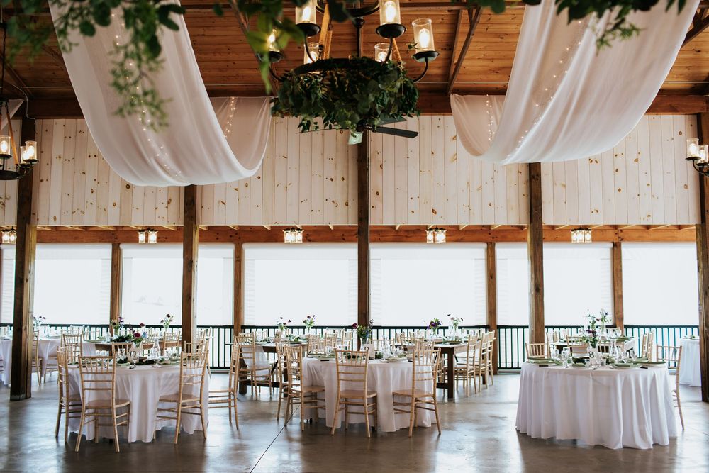 Elegant wedding reception hall with white drapes, exposed wooden beams, and natural lighting.