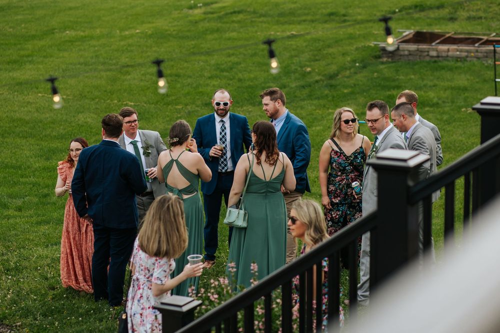 Wedding guests gathered on a grassy lawn near wooden fencing during outdoor reception.