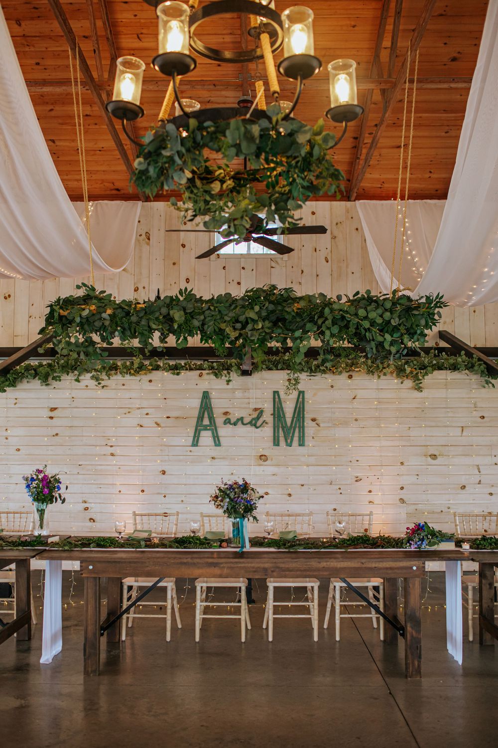 Rustic wedding venue interior with white brick walls, wooden beams and greenery decorations.