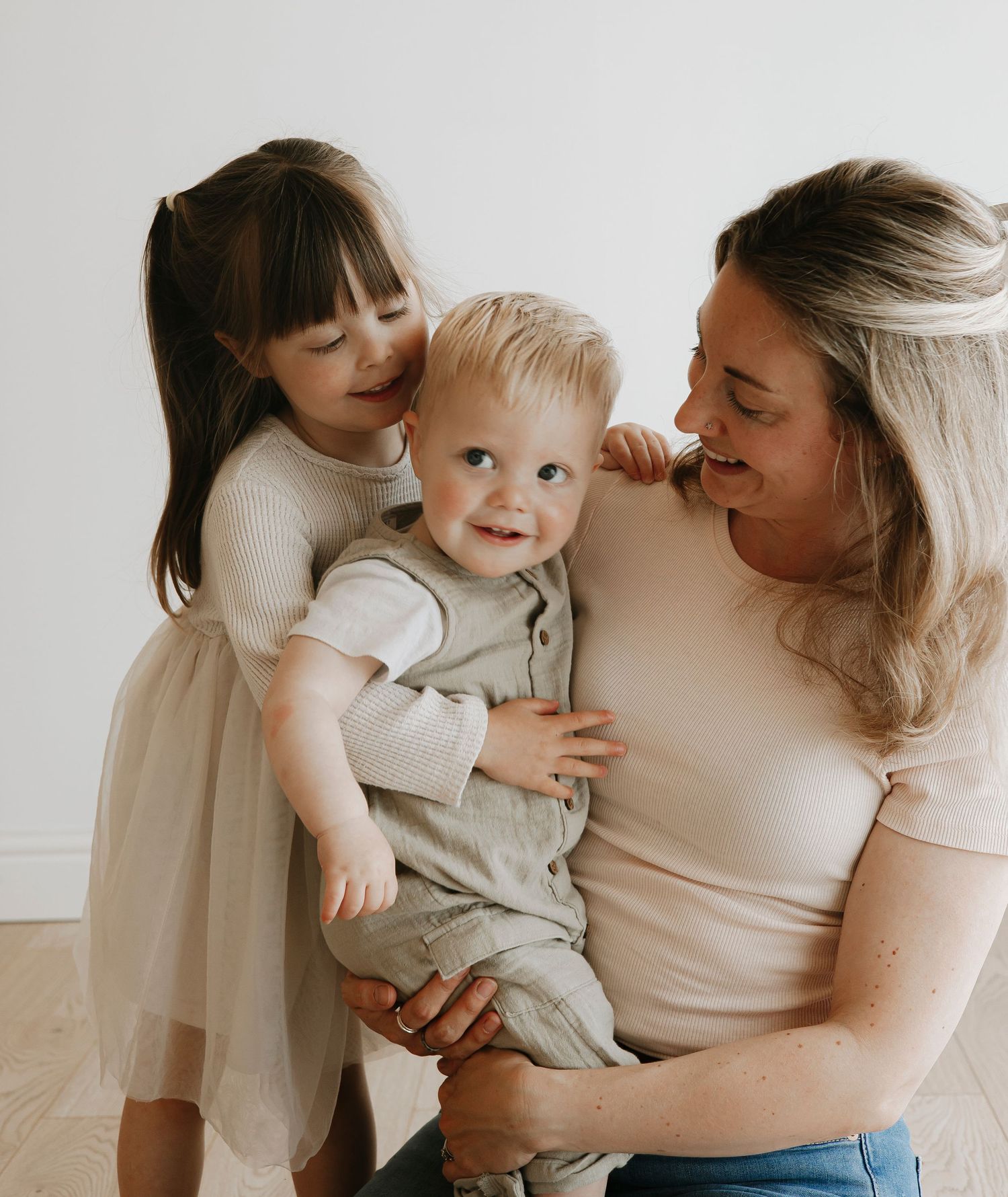 Sweet family moment captured with mother and child in neutral tones against white background.