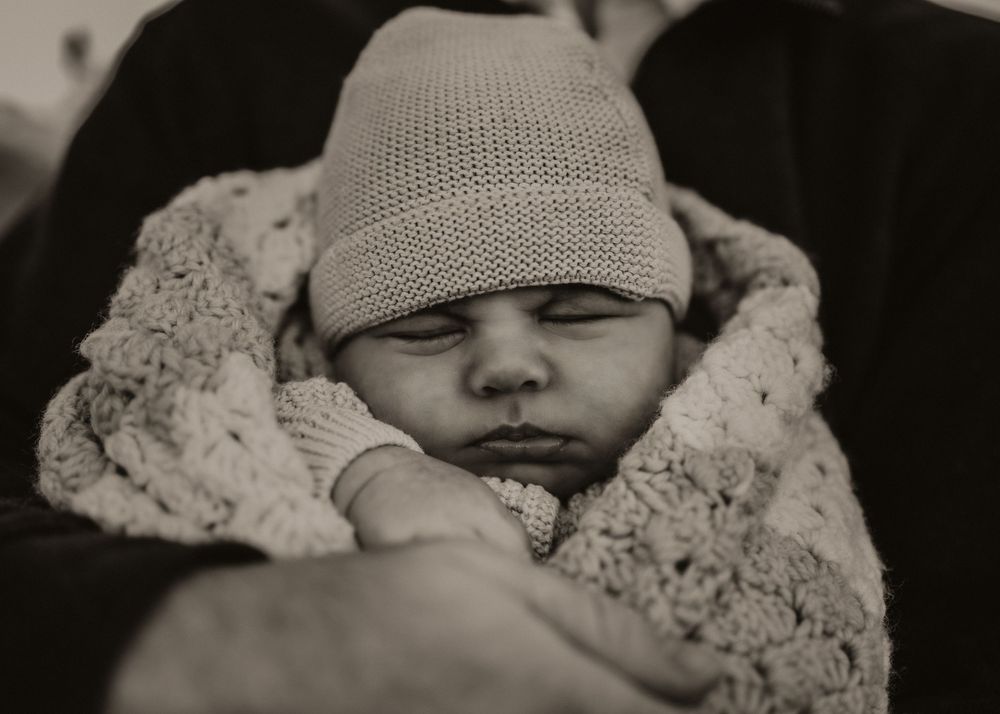 A black and white photo collage showing a sleeping baby wrapped in lace blankets wearing a knit cap.