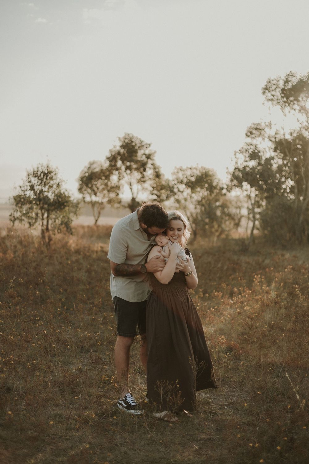 A parent and child share an intimate moment together in a golden sunset field with trees in the background.
