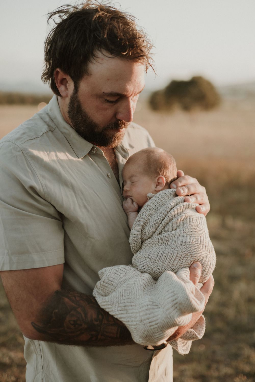 A tender moment captured in golden light as a parent cradles and kisses a swaddled newborn baby in a white knit blanket.