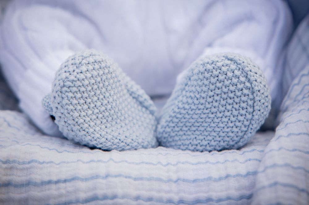 A series of light blue knitted baby booties arranged in a row against a soft textured background.