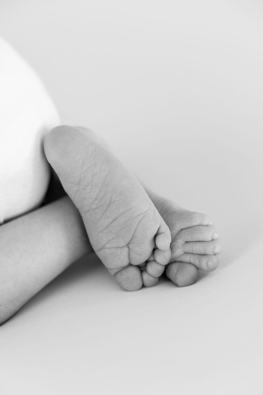Close-up black and white photo of tiny baby feet resting on a white surface.
