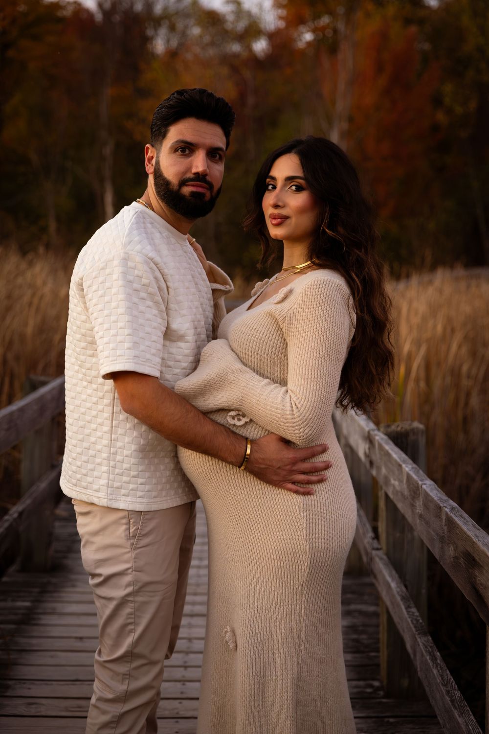 A couple embraces on a wooden boardwalk during an autumn maternity photoshoot at sunset.