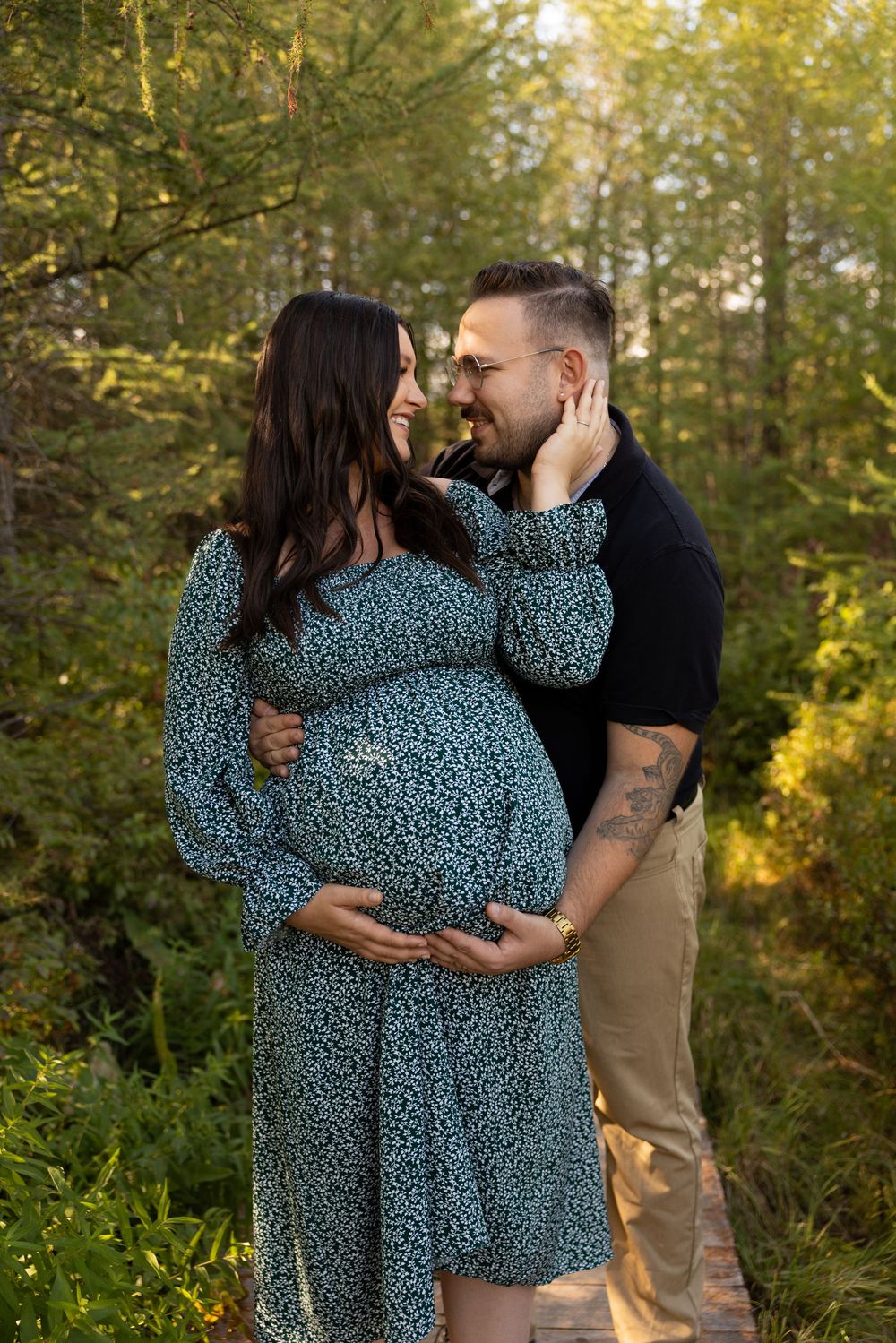 A couple shares an intimate moment in a wooded outdoor setting with golden sunlight filtering through the trees.