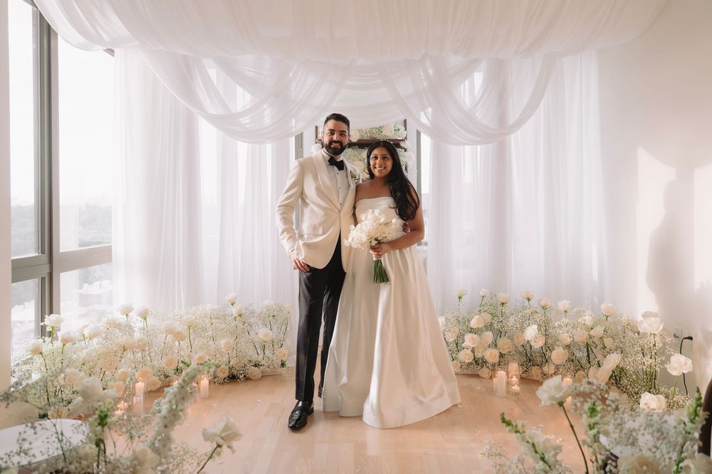 Wedding venue decorated with flowing white fabric and scattered floral arrangements on floor.