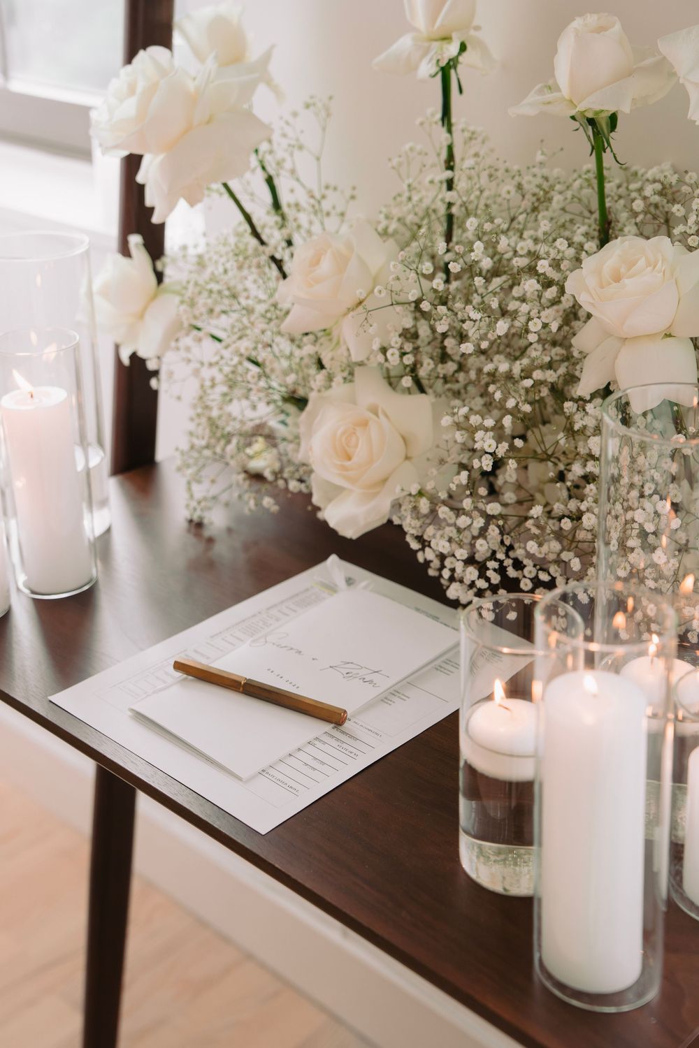 White roses and baby's breath centerpieces with lit candles on dark wood table.