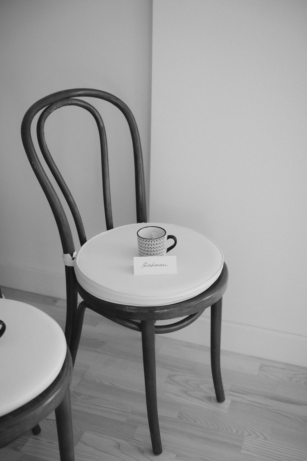 Minimalist black and white photo of wooden chairs with a coffee cup on white seat in an empty room.