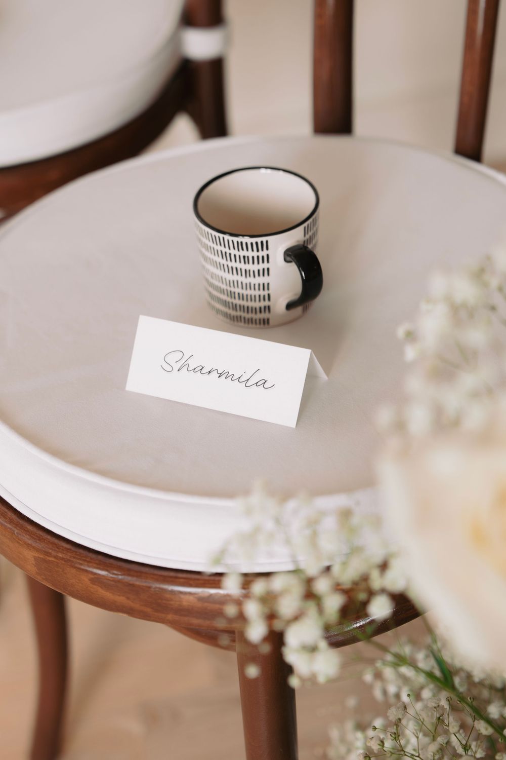 Place cards and delicate floral arrangements on white chairs for wedding ceremony setup.