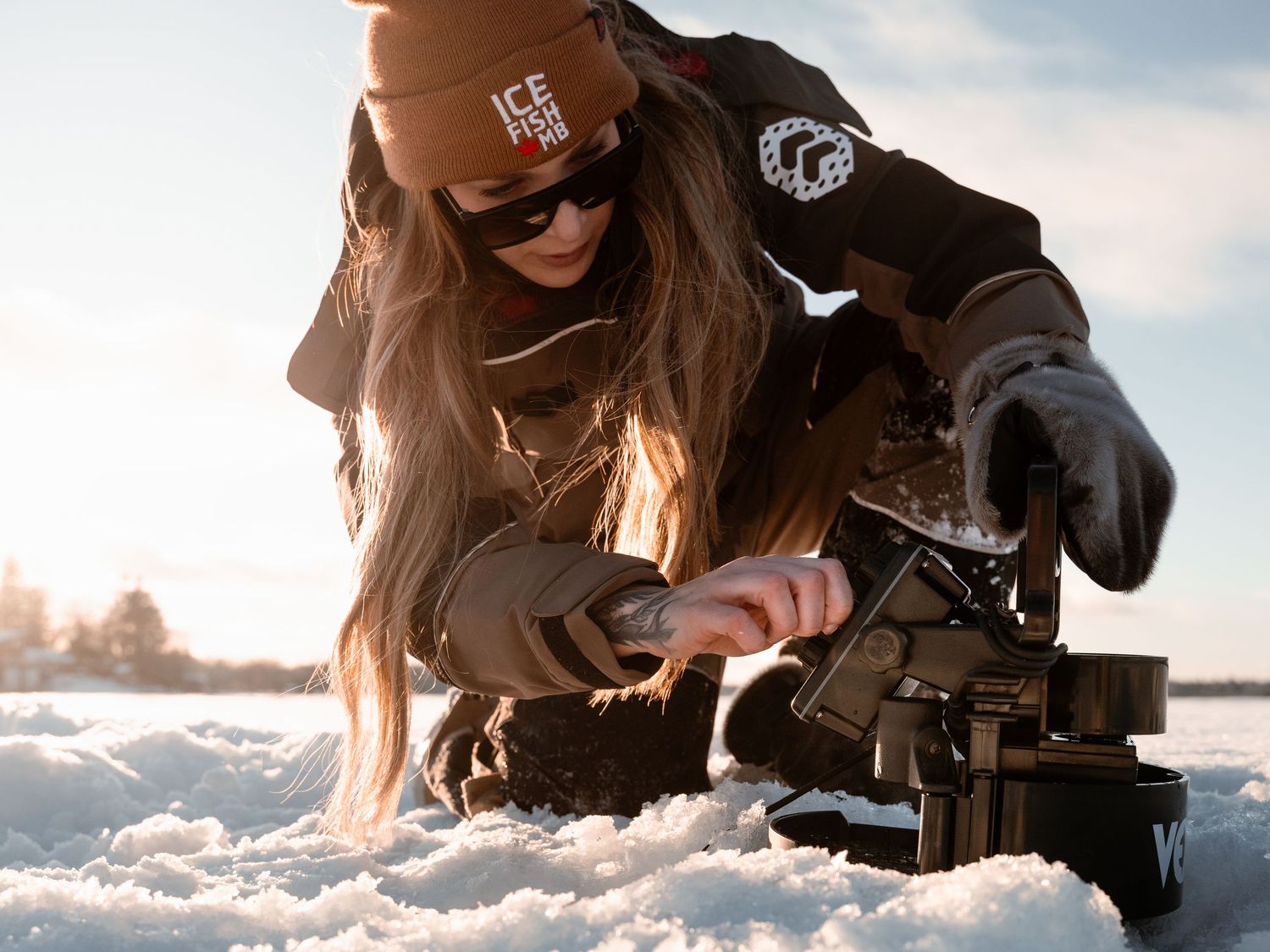 Close-up shot of winter fishing gear being prepared in snowy conditions at sunset.