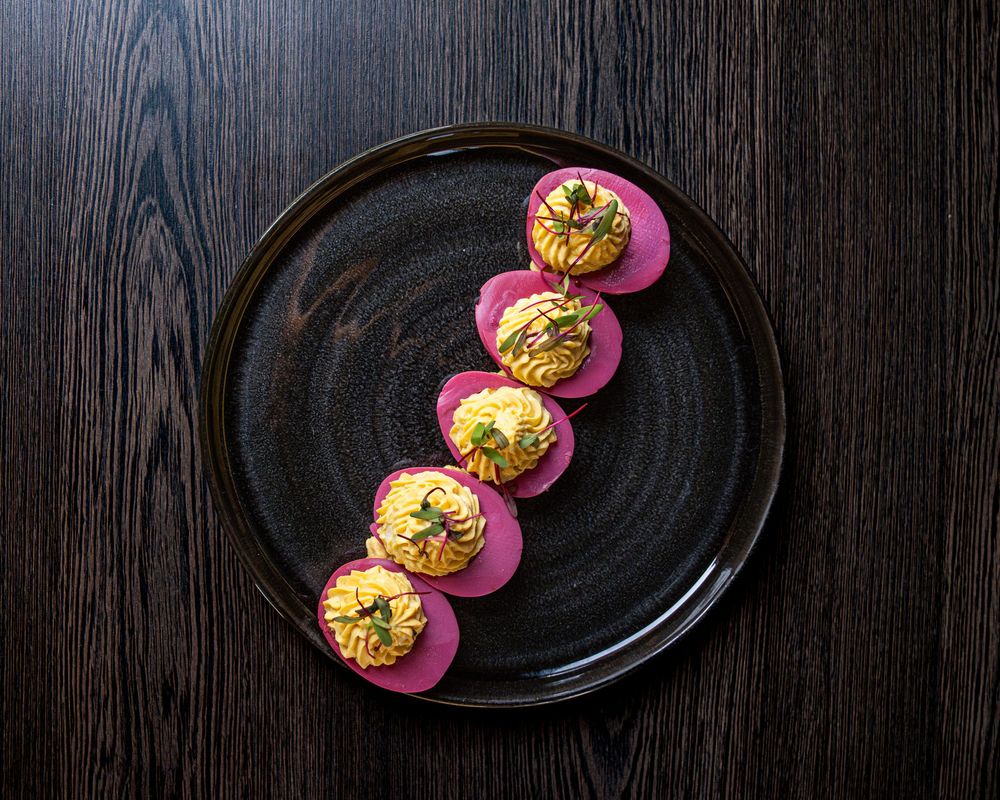 Elegant sushi rolls on pink rounds, artfully arranged on a black ceramic plate against a dark wood surface.