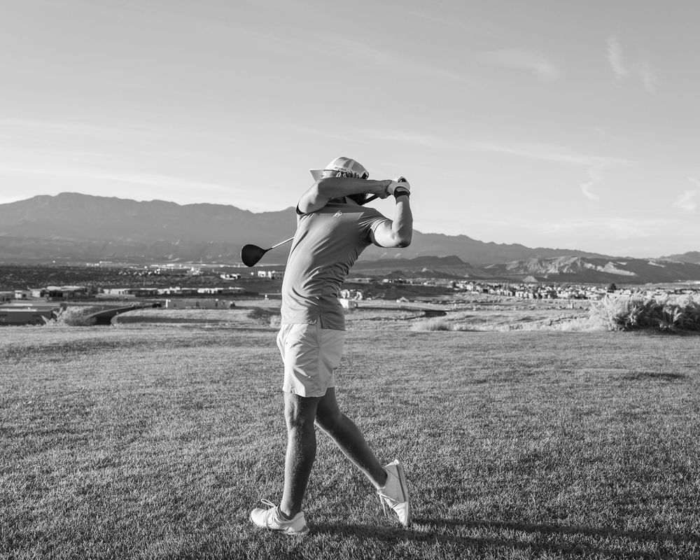 Black and white photo of a golfer completing a swing on a scenic golf course with mountains in the background.