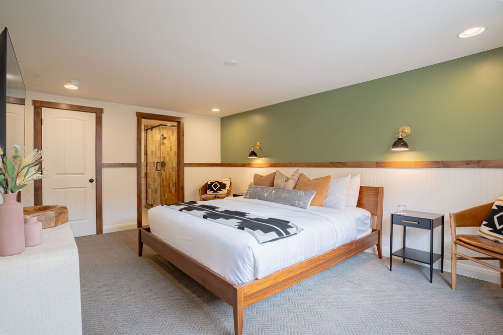 Modern hotel bedroom with green accent wall, wooden bed frame, and contemporary furnishings.