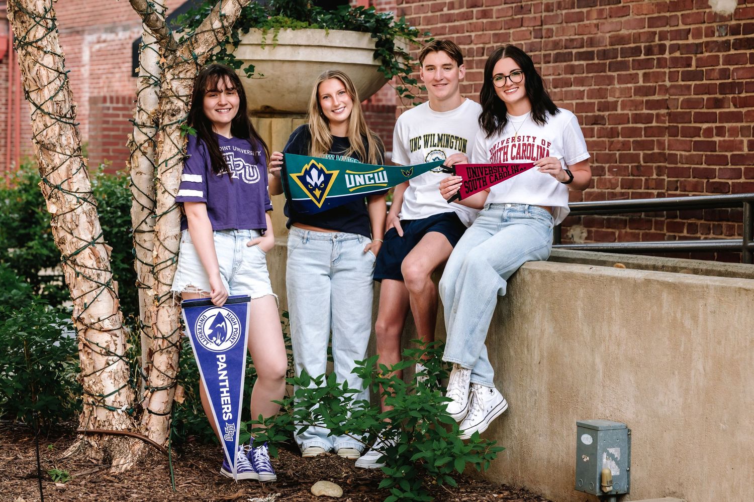 Group of friends sitting casually on outdoor brick steps wearing college sweatshirts and casual attire.