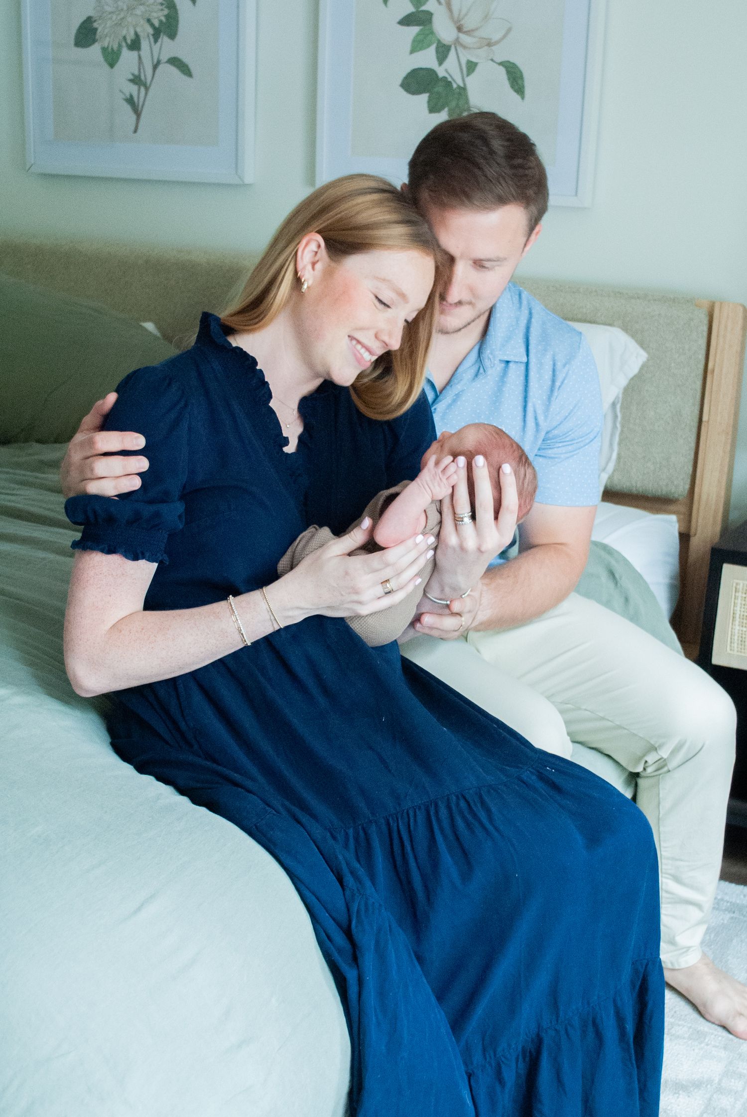 New Mom and dad in Wrightsville beach, NC sitting together on the edge of their bed admiring their precious newborn baby boy.