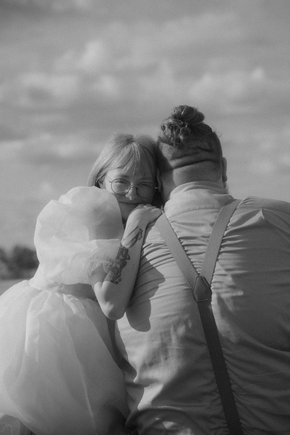 A romantic black and white photo of a couple embracing outdoors under cloudy skies.