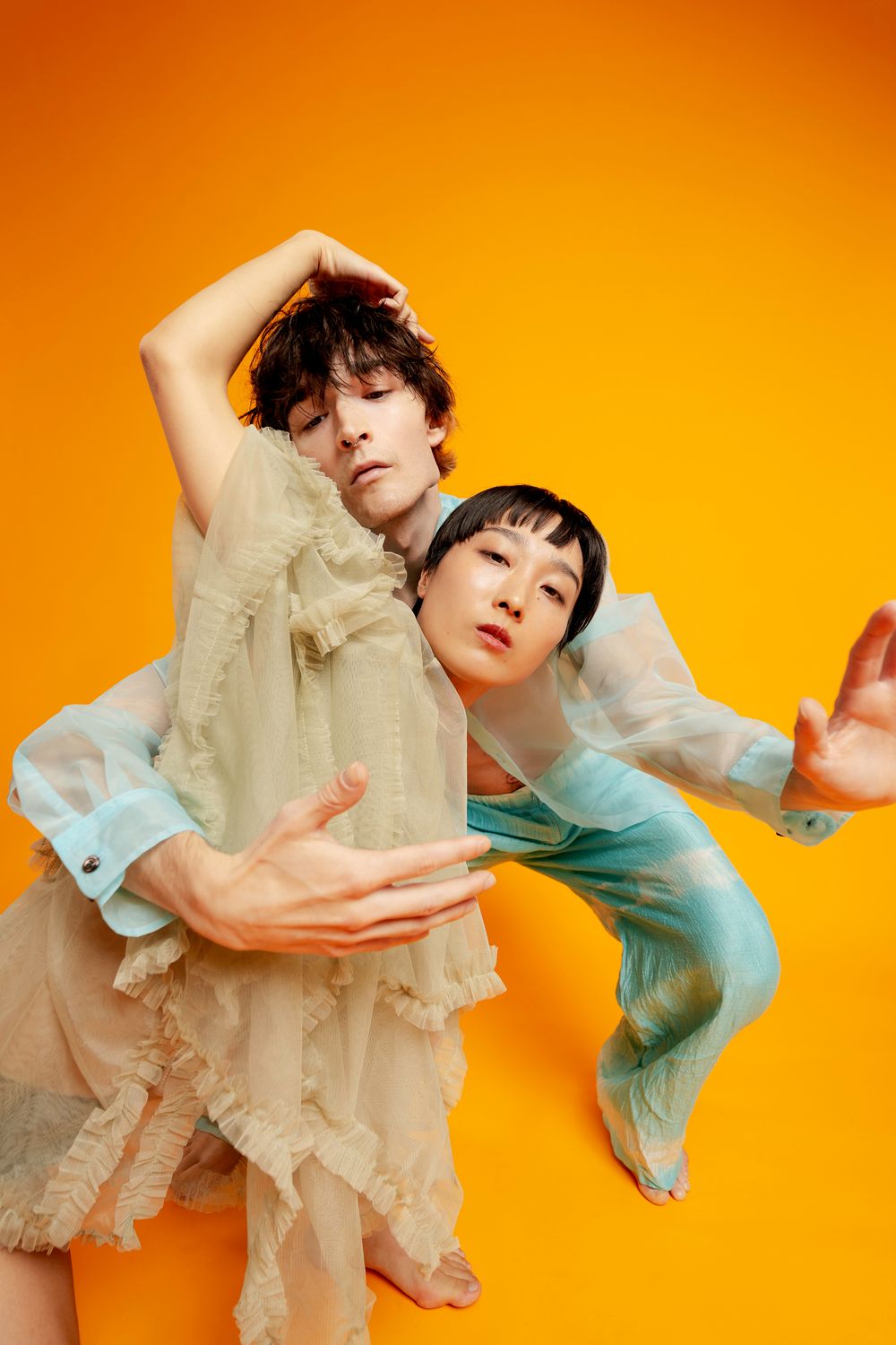 Artistic fashion portrait against orange backdrop showing flowing movement in light colored clothing.