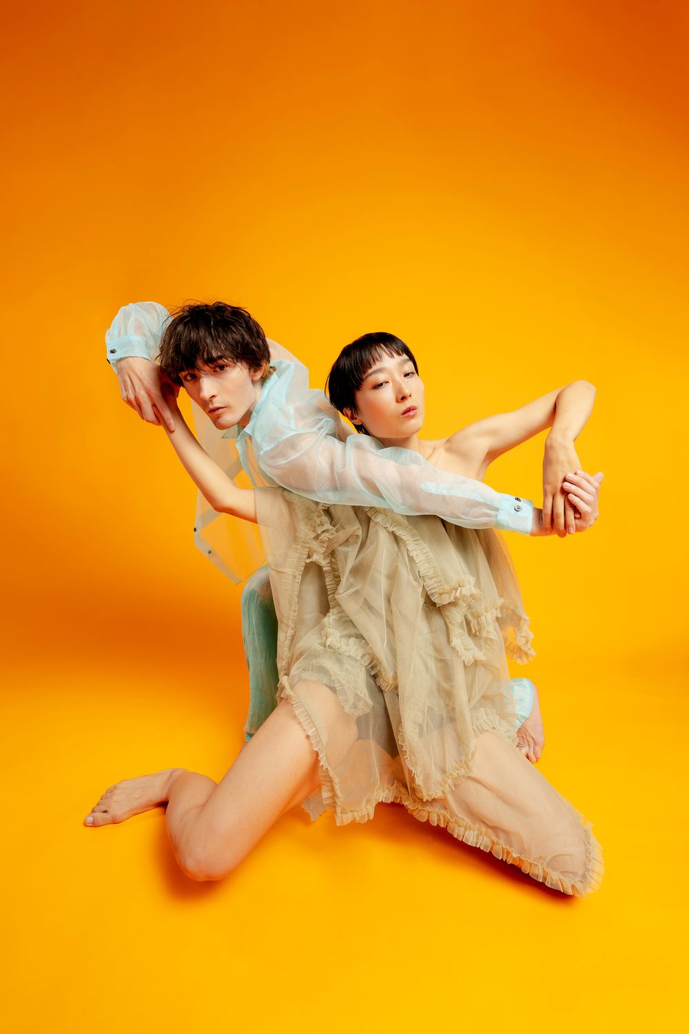 Artistic photo sequence showing a figure in flowy beige dress performing graceful movements against orange backdrop.