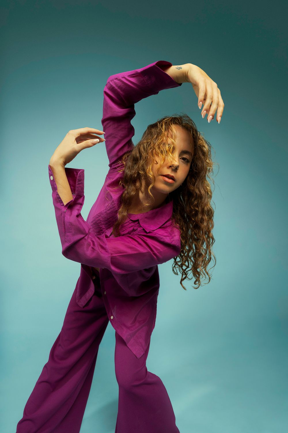 Dynamic fashion poses in purple attire against teal background showcasing fluid movement and style.