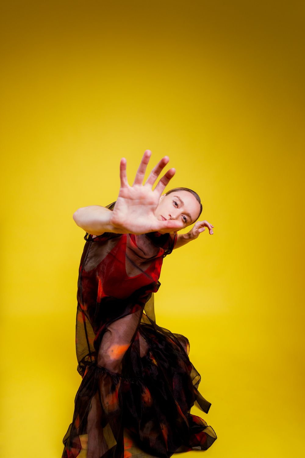 Dancer in flowing black dress performs expressive movement sequence against vibrant yellow backdrop.