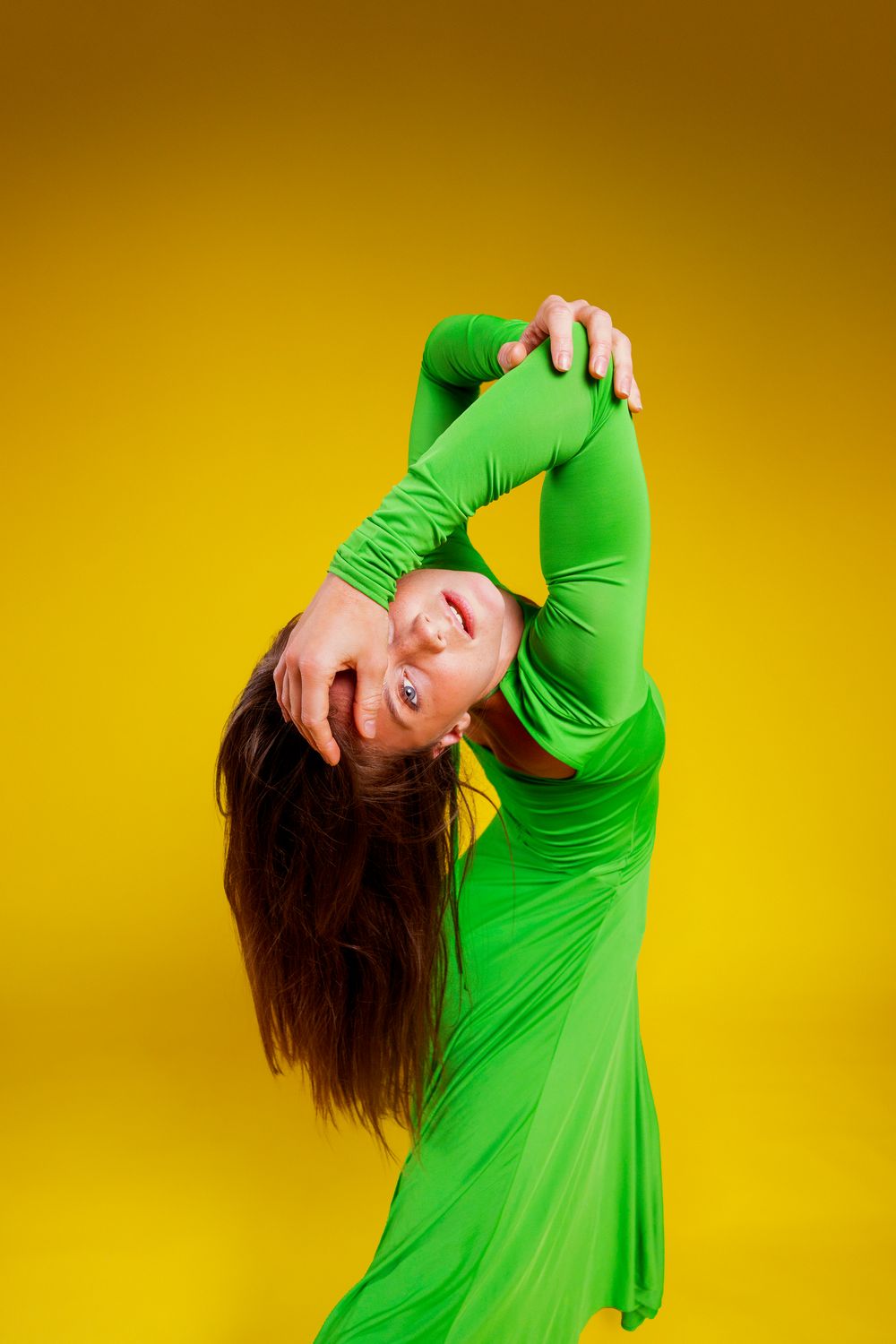 A dancer in bright green performs an expressive movement sequence against a vibrant yellow backdrop.