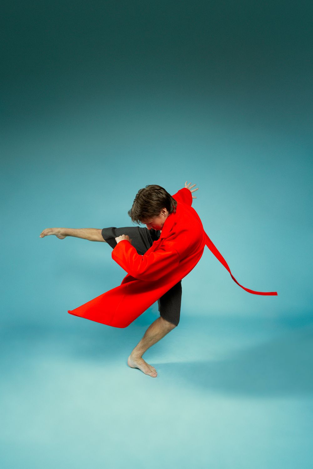 A graceful dancer in red fabric leaps through the air against a turquoise studio background.