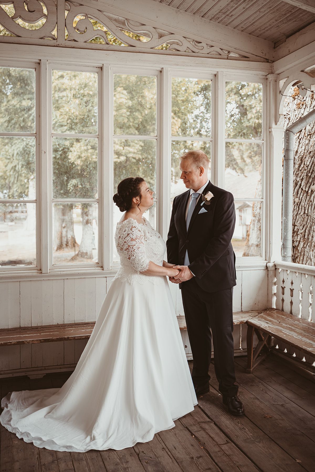 Brudpar ståendes på en vacker veranda med snickarglädje och dekorativa spröjsade fönster. Medevi Brunn, bröllopsfotograf Lets Bloom Media.