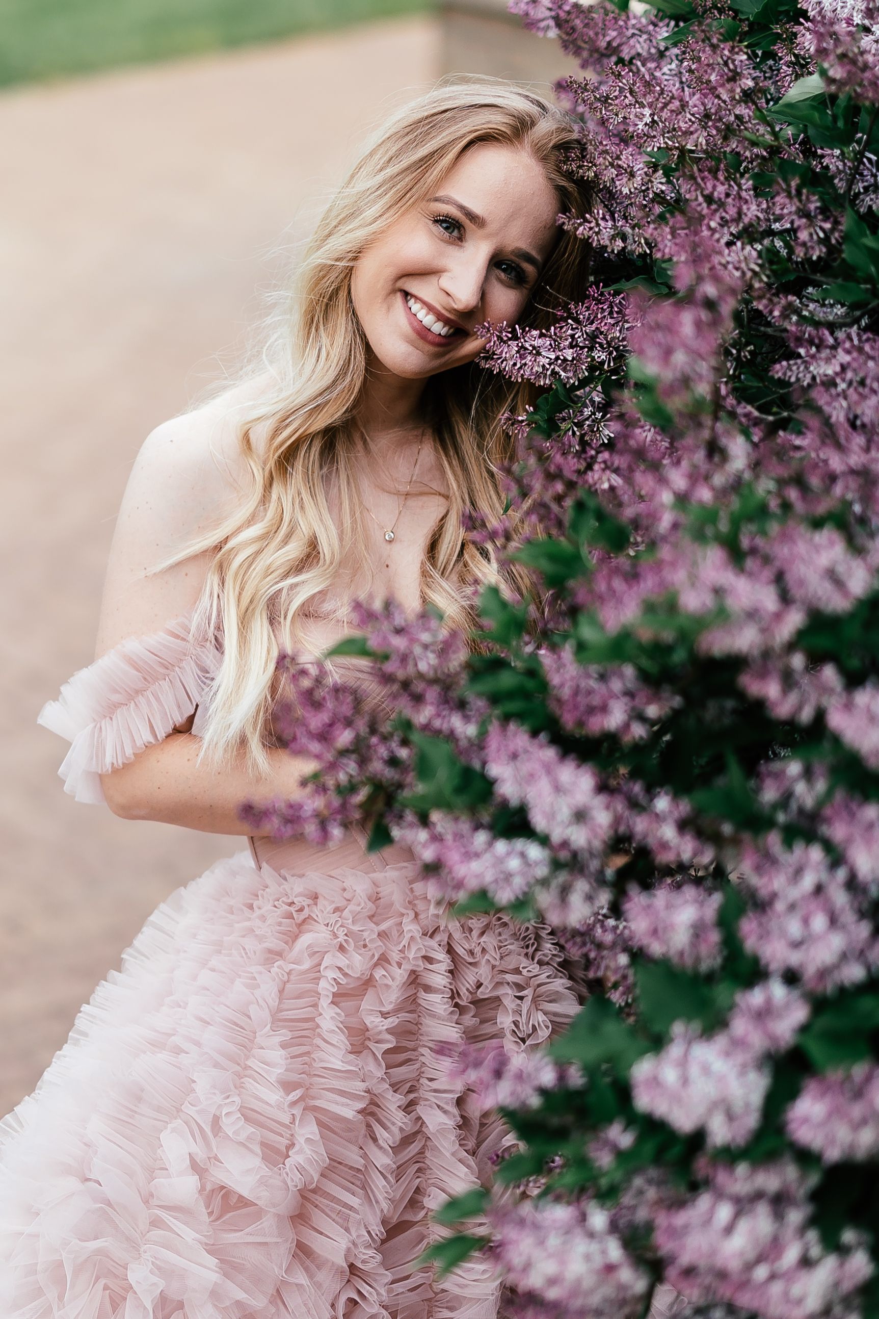 A springtime portrait session featuring a pink ruffled dress surrounded by blooming lilac flowers in soft natural light.