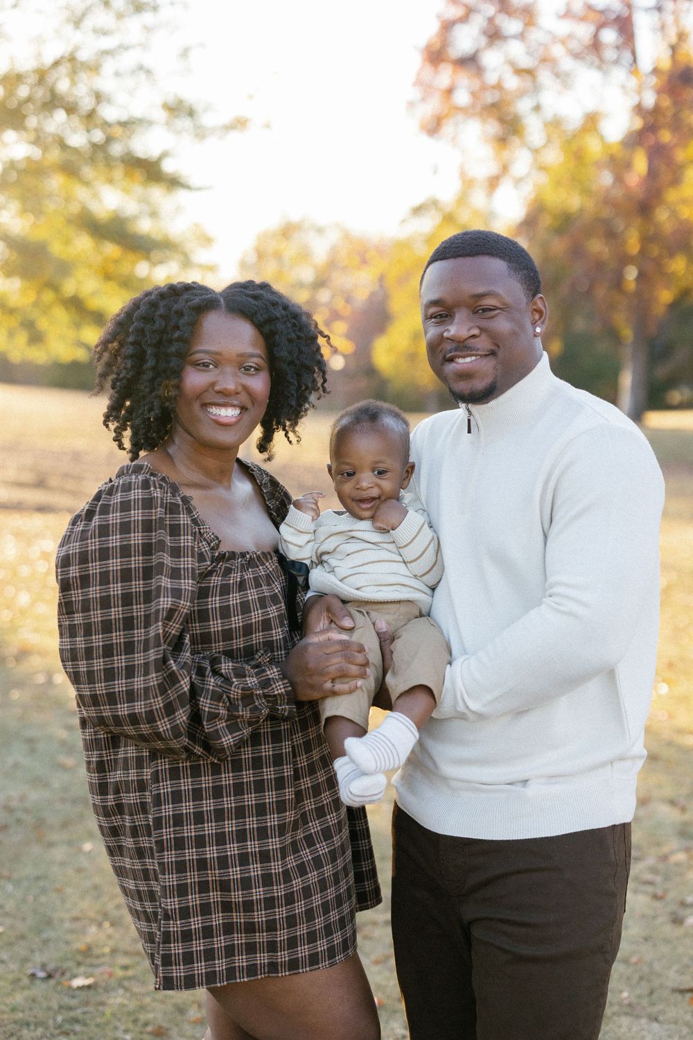 A family shares joyful moments together on a sunny autumn day in a park with golden foliage.